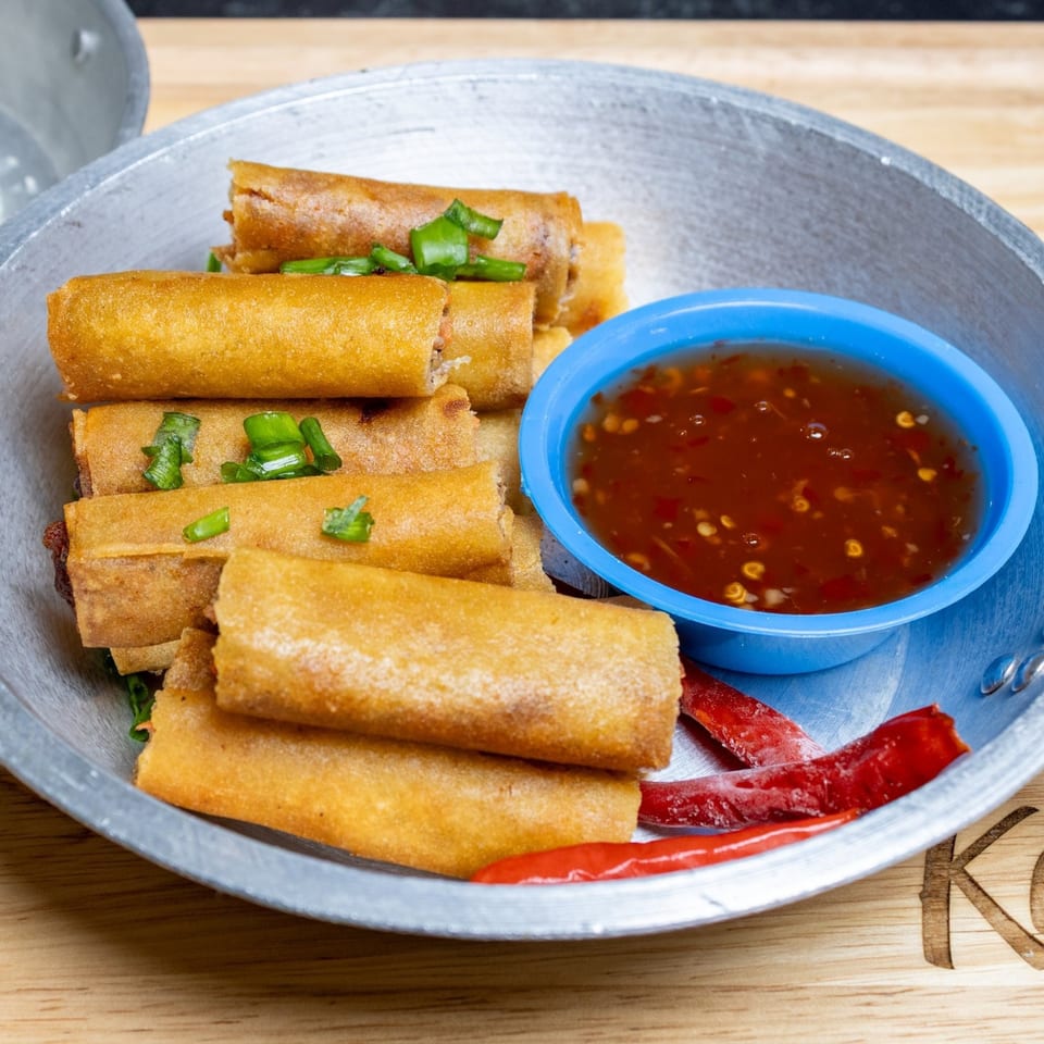 Filipino lumpia spring rolls with green onions, red chilies, and a side of dipping sauce.