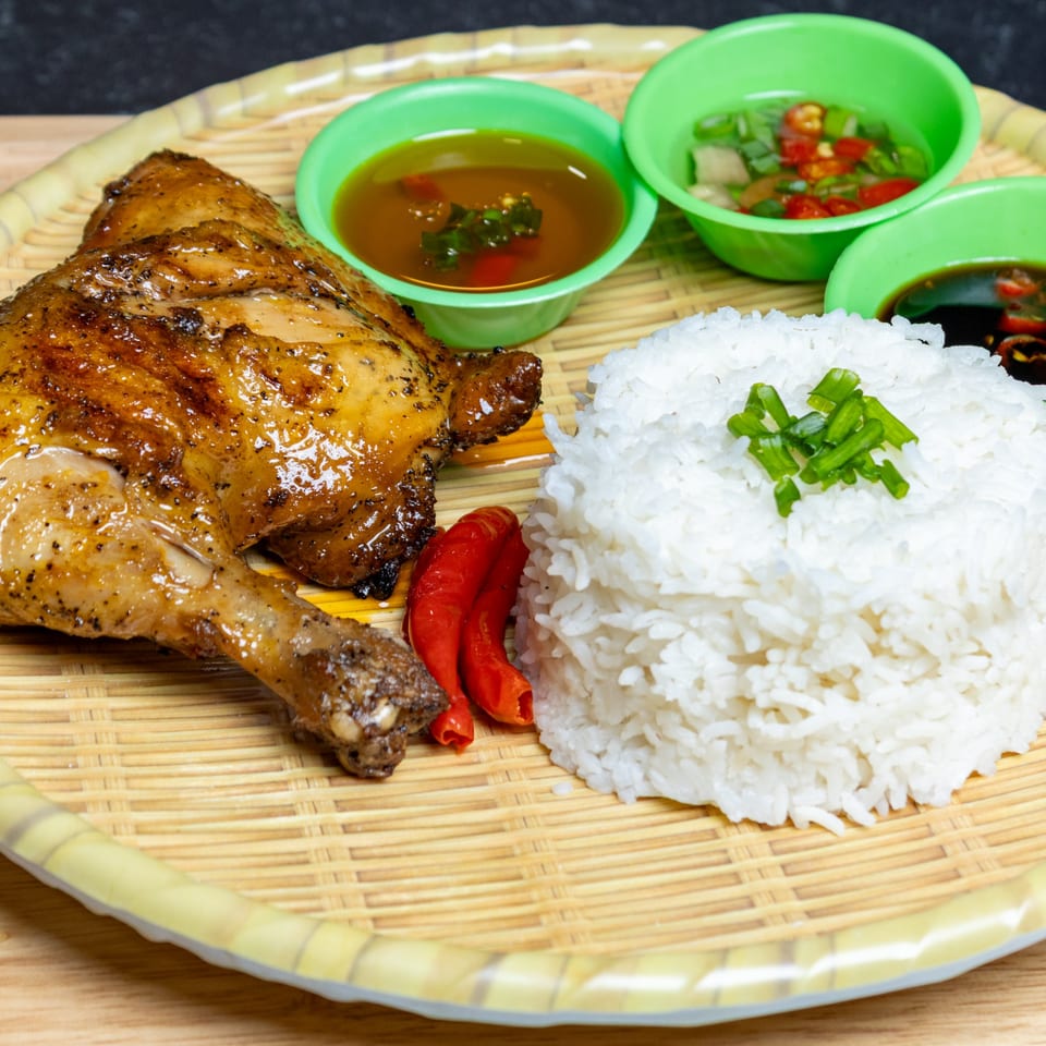 Filipino grilled chicken with white rice, red chilies, and three dipping sauces on a woven tray.
